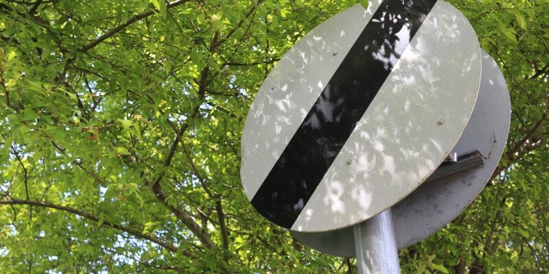 UK national speed limit road sign with trees behind
