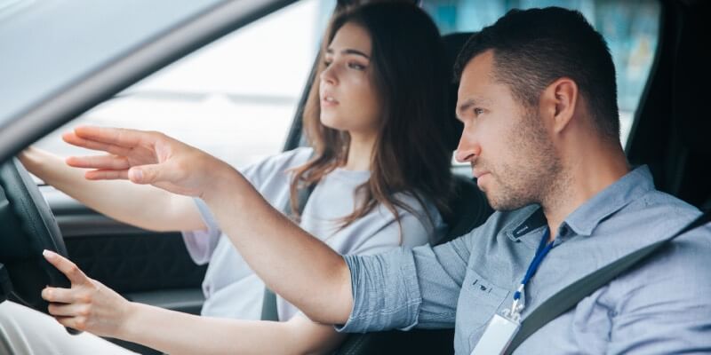 Girl driving, with man instructing her and pointing ahead