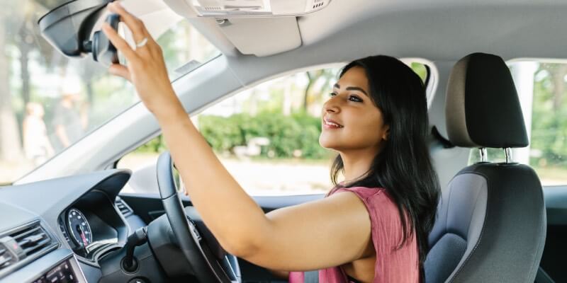 Woman smiling and adjusting her rearview mirror in the car