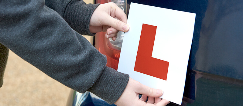 Two hands placing an l-plate onto rear of a car